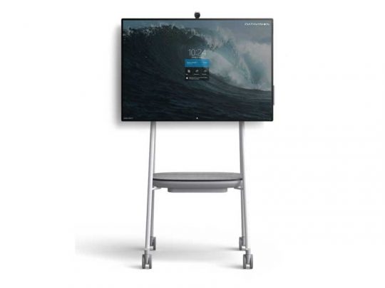 Microsoft Surface Hub 2S 50.5 Inch Whiteboard on a mobile stand with a large digital touchscreen display showing a desktop interface, time, and ocean wave background; includes a convenient shelf below the screen for accessories.