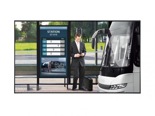 Businessman at a modern bus stop with suitcase, checking his phone; digital display board shows bus routes and times, parked city bus nearby, and tree-lined street in background. Public transportation travel concept.