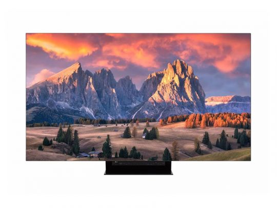 Flat-screen TV displaying a vivid mountain sunset scene with orange clouds, rocky peaks, green landscape, trees, and small houses in the foreground—perfect for showcasing 4K Ultra HD television picture quality.