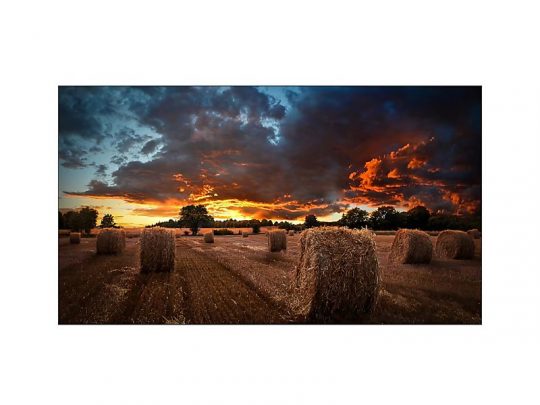 Das Samsung VM46B-U Videowall Display (46 Zoll, Neuware) zeigt ein beeindruckendes Landschaftsbild mit dramatischem Sonnenuntergang, runden Heuballen auf einem Feld, dunklen Wolken und fernen Bäumen - ideal für hochwertige Präsentationen und brillante Farbdarstellung.