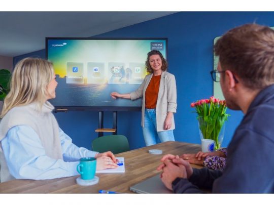 Eine Frau präsentiert ihre zwei Kollegen mithilfe eines 55 Zoll Touchdisplays, dem Legamaster EVOLVE 2 ETX-5540 (Neuware), in einem modernen Büro. Auf dem Tisch liegen Notizbücher, Tassen und Dekoration - ideal zum Kaufen oder Mieten für Meetings und Präsentationen.